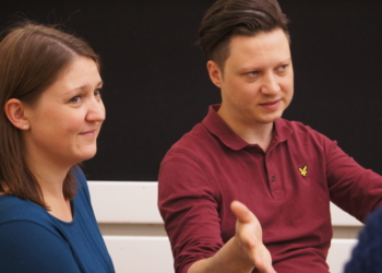 Frau und Mann im Gespräch mit Zuhörenden