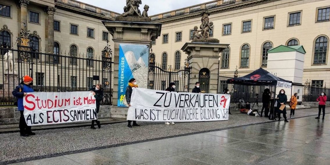Berliner Studierende stehen mit Protestplakaten vor einem Universitätsgebäude. Auf einem großen Banner steht "Zu Verkaufen".